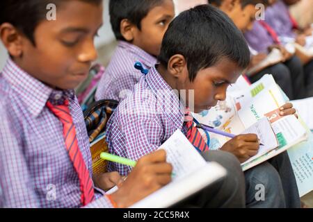 Gli studenti delle scuole elementari in uniforme frequentano la scuola insieme e studiano con libri di testo e strumenti di scrittura a Bihar, India. Foto Stock