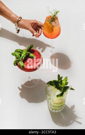 Popolari cocktail alcolici estivi al bar. Gin-tonic, Aperol Spritz e Margarita al basilico alla fragola in bicchieri e donne che raggiungono a mano per il vetro sopra Foto Stock