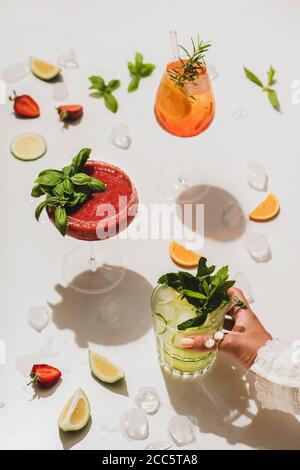 Popolari cocktail alcolici estivi al bar. Gin-tonic, Aperol Spritz e Margarita al basilico di fragola in bicchieri e donne che tengono il vetro a mano su pirai Foto Stock