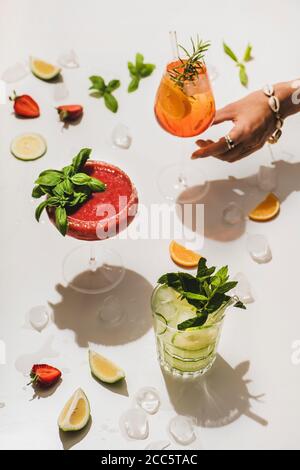 Popolari cocktail alcolici estivi al bar. Gin-tonic, Aperol Spritz e Margarita al basilico alla fragola in bicchieri e donne che raggiungono a mano per il vetro sopra Foto Stock