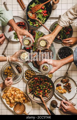 Festa estiva con barbecue. Piatto-lay di tavola con carne alla griglia, verdure, insalata, patate arrosto e mani di popoli che si festeggiano su tovaglia scacchi, a. Foto Stock