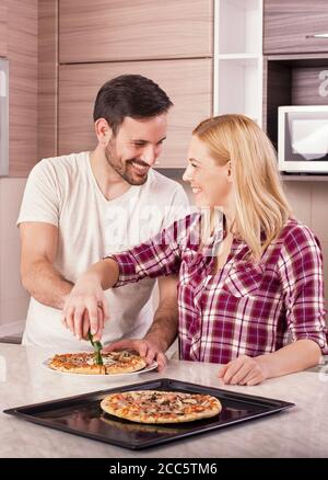 Immagine verticale di una coppia felice che fa la pizza fatta in casa dentro la cucina Foto Stock
