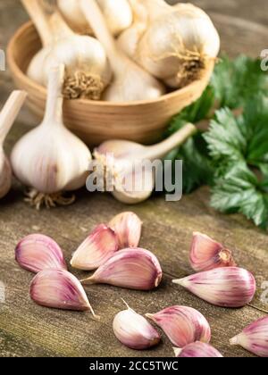 Spicchi d'aglio e bulbi freschi e foglie di sedano maturi in ciotola e vecchio tavolo di legno d'annata. Cibo biologico sano, vitamine, viands BIO, backgro naturale Foto Stock