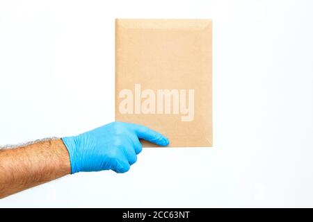 Primo piano una mano del corriere maschile in un guanto medico tiene una busta su sfondo bianco. Mano di Mailman che consegna la posta. Spedizione pacchi Foto Stock