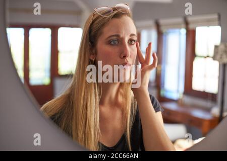 Riflessione di donna che controlla la sua pelle nello specchio a casa Foto Stock