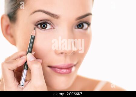 Donna asiatica che si prepara ad applicare la matita occhio eyeliner marrone sugli occhi che guardano nello specchio. Isolato su sfondo bianco Foto Stock