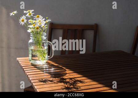 Bouquet di margherite selvatiche in vaso di vetro su tavolo di legno in giornata di sole Foto Stock