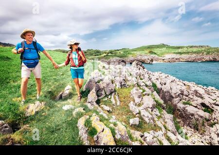 Un paio di viaggiatori zaino in spalla cammina sulla costa rocciosa dell'oceano. Asturie. Spagna Foto Stock