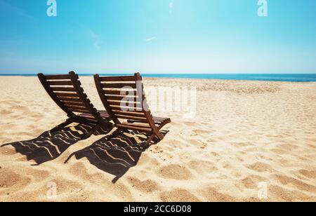 Due sedie da spiaggia sulla spiaggia vuota dell'oceano sotto il sole luminoso Foto Stock