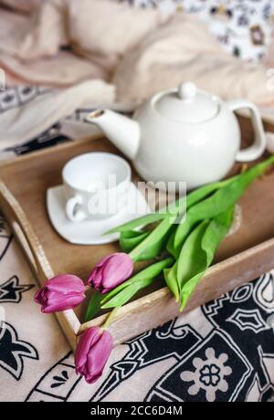 Tulipani con teiera e tazza sono su vassoio in camera da letto Foto Stock