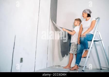 Madre e figlio staccano i wallpapers dal muro e preparano camera per ristrutturazione Foto Stock