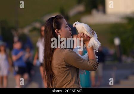 Giovane ragazza in piedi su una strada che tiene due colombe nelle mani e che dice qualcosa a loro, gente offuscata su uno sfondo. 4 giugno 2019. Kiev, Ucraina Foto Stock