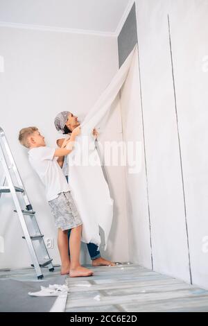 Madre e figlio prendono insieme gli sfondi e preparano la stanza per lavori di ristrutturazione Foto Stock