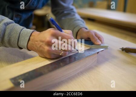 Vista di un falegname con una matita per disegnare una linea su una tavola di legno. Foto Stock