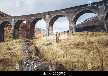 Escursione, passeggiata con zaino, stile di vita attivo concept immagine. Uomo viaggiatore cammina neaar famoso Glenfinnan viadukt in Scozia Foto Stock