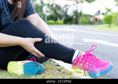 Donna asiatica massaggiando il suo dolore di vitello dal jogging e correre all'esterno al parco. Lesioni da sport e concetto di esercizio. Foto Stock
