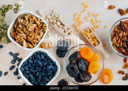 Frutta secca, noci e semi in ciotole su fondo beige chiaro Foto Stock