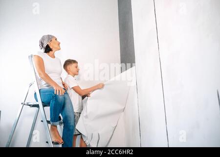 Madre e figlio prendono insieme gli sfondi e preparano la stanza per lavori di ristrutturazione Foto Stock