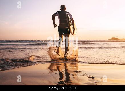 Surfista con surf corre alle onde oceaniche Foto Stock