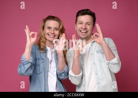 Uomo e donna sorridenti dal bell'aspetto che mostrano il segno OK con due mani. Foto Stock