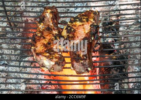 Le bistecche di maiale marinate in salsa su costolette vengono fritte su calici su una griglia di metallo in un picnic. Sfondo. Foto Stock