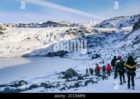 Linea di persone che camminano sul ghiacciaio Sólheimajökull in inverno, uno sbocco del ghiacciaio Mýrdalsjökull, Islanda Foto Stock