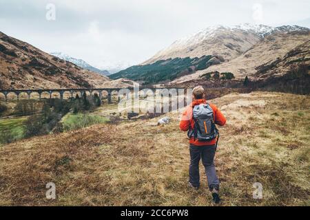 Escursione, passeggiata con zaino, stile di vita attivo concept immagine. Uomo viaggiatore cammina neaar famoso Glenfinnan viadukt in Scozia Foto Stock