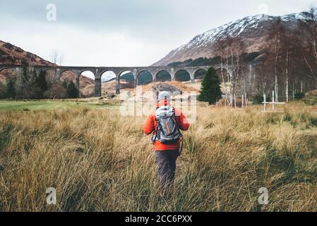 Escursione, passeggiata con zaino, stile di vita attivo concept immagine. Uomo viaggiatore cammina neaar famoso Glenfinnan viadukt in Scozia Foto Stock