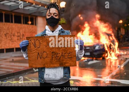 Seattle, USA 30 maggio 2020: Un attivista con un cartello NO JUSTICE NO PEACE, mentre un'auto della polizia brucia sullo sfondo a Westlake. Foto Stock