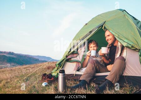 Immagine del concetto di lisure familiare. Padre e figlio bevono un tè seduto in tenda turistica Foto Stock