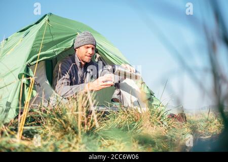 L'uomo si siede in tenda e beve il tè caldo Foto Stock