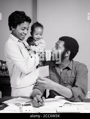 ANNI '70 SORRIDENTE AFROAMERICANO FAMIGLIA MADRE BAMBINO IN ARMI CON CUI PARLARE PADRE SEDUTO AL TAVOLO DI REVISIONE DELLE BOLLETTE E DEL BUDGET DI FAMIGLIA - B26004 HAR001 HARS COPPIA MADRI VECCHIO TEMPO NOSTALGIA VECCHIO MODO BARBA 1 FAMIGLIA GIOVANILE COMUNICAZIONE LAVORO DI SQUADRA BAMBINI BAMBINI SODDISFATTI FAMIGLIE GIOIA STILE DI VITA FEMMINE SPOSATO CONIUGE MARITI SALUTE HOME VITA COPIA SPAZIO AMICIZIA MEZZA LUNGHEZZA SIGNORE PERSONE MASCHI PADRI B&W PARTNER BAFFI FELICITÀ ALLEGRO BAFFI AFROAMERICANI AFROAMERICANI E PAPÀ NERO ETNIA VISO CAPELLI SORRISI CONNESSIONE REVISIONE BILANCI GIOIOSO BAMBINO LAVORO DI CARTA RAGAZZO BARBE Foto Stock