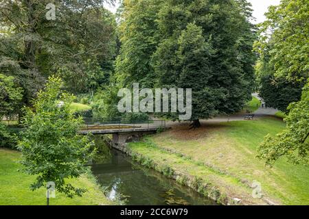 Ponte pedonale su un ruscello circondato da enormi alberi frondosi in un parco nella città di Maastricht, rilassante giorno d'estate Foto Stock