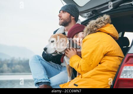 Padre e figlio con cane beagle che si siedono insieme nel bagagliaio dell'auto. Fine autunno Foto Stock