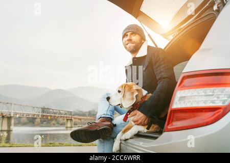 Uomo con cane beagle seduto insieme nel bagagliaio dell'auto. Fine autunno Foto Stock