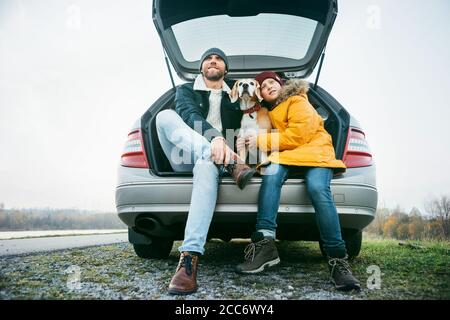 Padre e figlio con cane beagle che si siedono insieme nel bagagliaio dell'auto. Pausa lunga del viaggio. Foto Stock