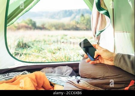 Il viaggiatore usa il telefono cellulare seduto in tenda. Primo piano immagine mani uomo con telefono cellulare Foto Stock