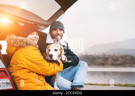 Padre e figlio con cane beagle che si siedono insieme nel bagagliaio dell'auto e sorridono in macchina fotografica. Foto Stock