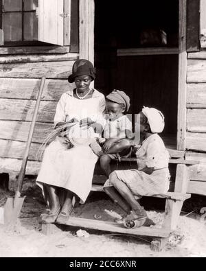 1930 LA MADRE AFROAMERICANA DI GULLAH TESSENDO UN CESTINO TURISTICO SEDUTO SOPRA PASSI A CABINA CON I SUOI DUE BAMBINI SOUTH CAROLINA USA - N1209 HAR001 HARS 3 ART TRAVEL MOM ABBIGLIAMENTO STRESS NOSTALGICO COPPIA BELLEZZA COMUNITÀ PASSI LE SUE MADRI VECCHIO TEMPO OCCUPATO NOSTALGIA FRATELLO VECCHIA MODA SORELLA POVERTÀ 1 GIOVANE STILE PERSO FIGLI FAMIGLIE STILE DI VITA FEMMINE CASE FRATELLI POVERI RURALE VITA DOMESTICA STATI UNITI COPY SPAZIO FULL-LENGTH DONNE FIGLIE PERSONE RESIDENZIALI UNITI STATI D'AMERICA CURA MASCHI EDIFICI BARACCA CRAFT FRATELLI B&W TRISTEZZA NORD AMERICA LIBERTÀ NORDAMERICANA ABILITÀ SOUVENIR Foto Stock