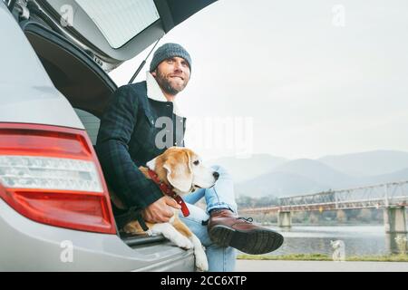 Uomo con cane beagle seduto insieme nel bagagliaio dell'auto. Nel tardo autunno viaggia con il concetto di animali domestici. Foto Stock