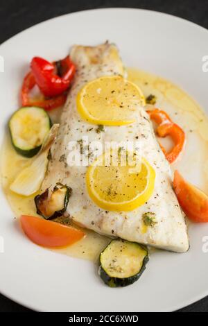 Un filetto di una linea catturato branzino selvatico, Dicentrarchus labrax, che è stato arrostito con verdure, fette di limone, olio d'oliva e burro e condito w Foto Stock