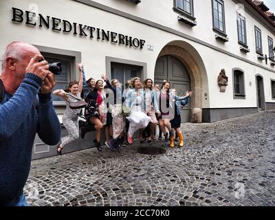 GUMPOLDSKIRCHEN, AUSTRIA - 09/01/2018. Felice sposa caucasica con bridesmaids che salta per strada. Matrimonio in stivali di gomma in giornata piovosa. Foto Stock