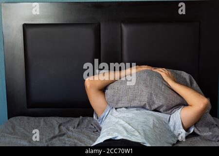 Giovane uomo ispanico con lunghi capelli ricci che prendono un pisolino su un letto con lenzuola grigie Foto Stock