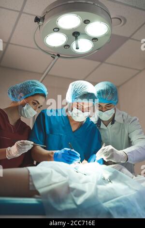 Gruppo di chirurghi al lavoro che operano in sala operatoria. Medicina di rianimazione team indossando maschere di protezione tenendo in acciaio strumenti medici salvataggio patie Foto Stock