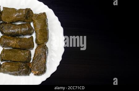 Foglie d'uva ripiene su piatto bianco su sfondo di legno scuro con spazio per la copia. Famosa cucina tradizionale mediorientale, turca, asiatica. Dolma o stuffe Foto Stock