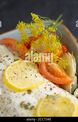 Un filetto di una linea catturato branzino selvatico, Dicentrarchus labrax, che è stato arrostito con verdure, fette di limone, olio d'oliva e burro e condito w Foto Stock