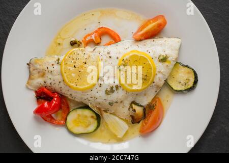 Un filetto di una linea catturato branzino selvatico, Dicentrarchus labrax, che è stato arrostito con verdure, fette di limone, olio d'oliva e burro e condito w Foto Stock