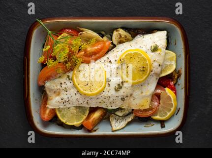 Un filetto di una linea catturato branzino selvatico, Dicentrarchus labrax, che è stato arrostito con verdure, fette di limone, olio d'oliva e burro e condito w Foto Stock