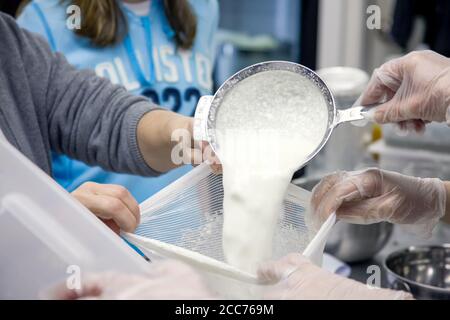 Le donne che si accovacciano le cagliate (versando / raccogliendo la cagliata morbida di formaggio di capra in contenitori o sacchetti di stoffa di formaggio durante una classe di cheesemaking in città di caduta, W. Foto Stock