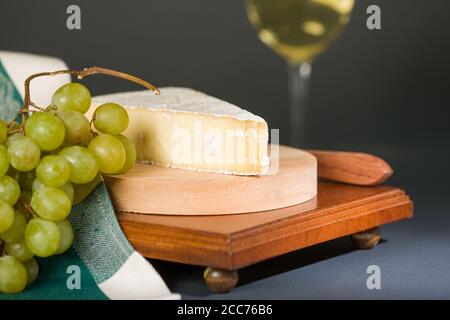 Baby Brie affumicato con uva, tovagliolo e bicchiere di vino chardonnay Foto Stock